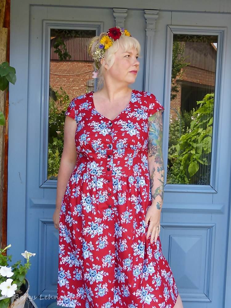 dirndlkleid sissi gr. 32 50 Frau in geblümtem Kleid vor blauer Tür stehend.