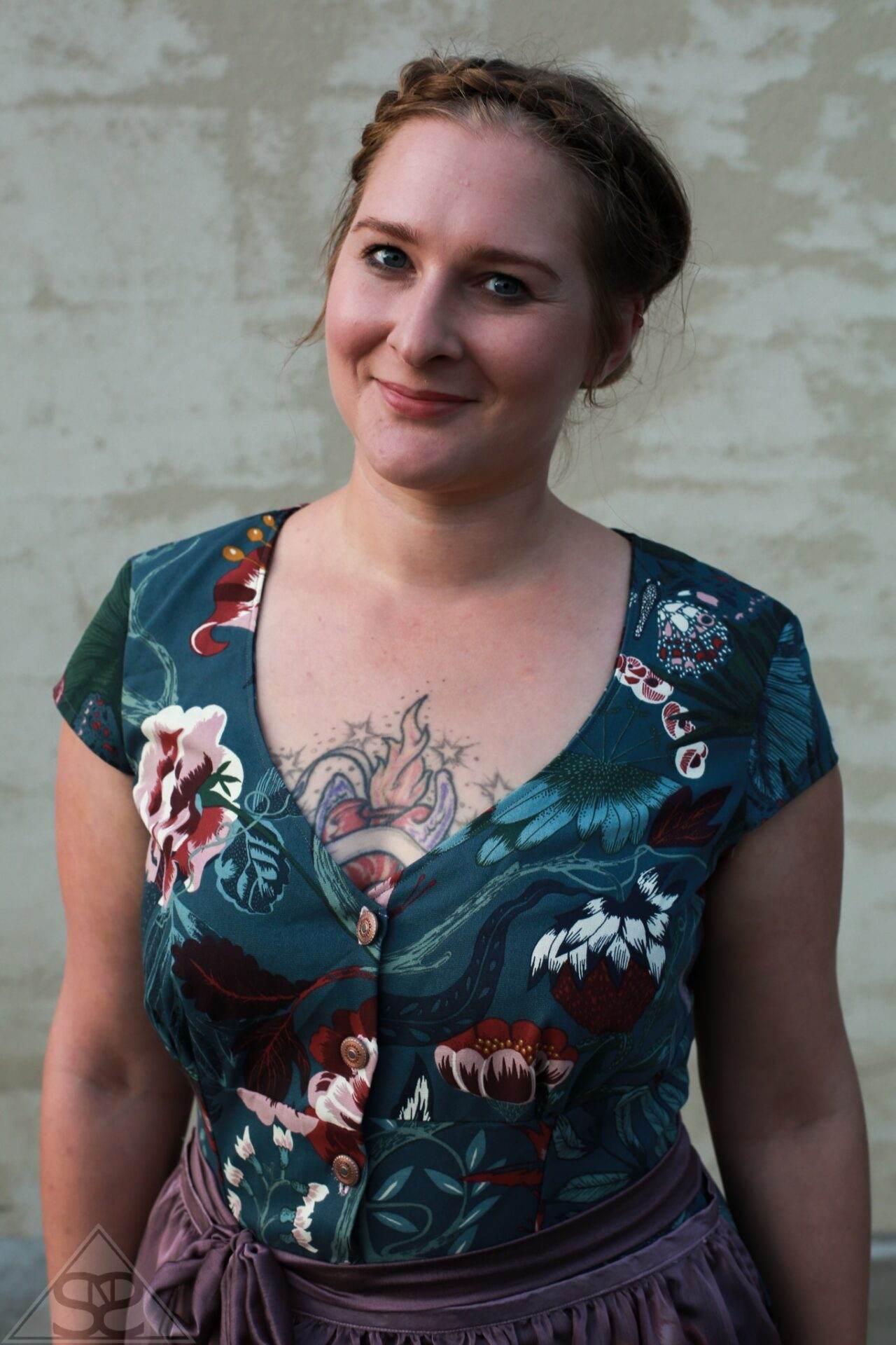 dirndlkleid sissi gr. 32 50 Person mit floralem Oberteil und Brusttattoo lächelt