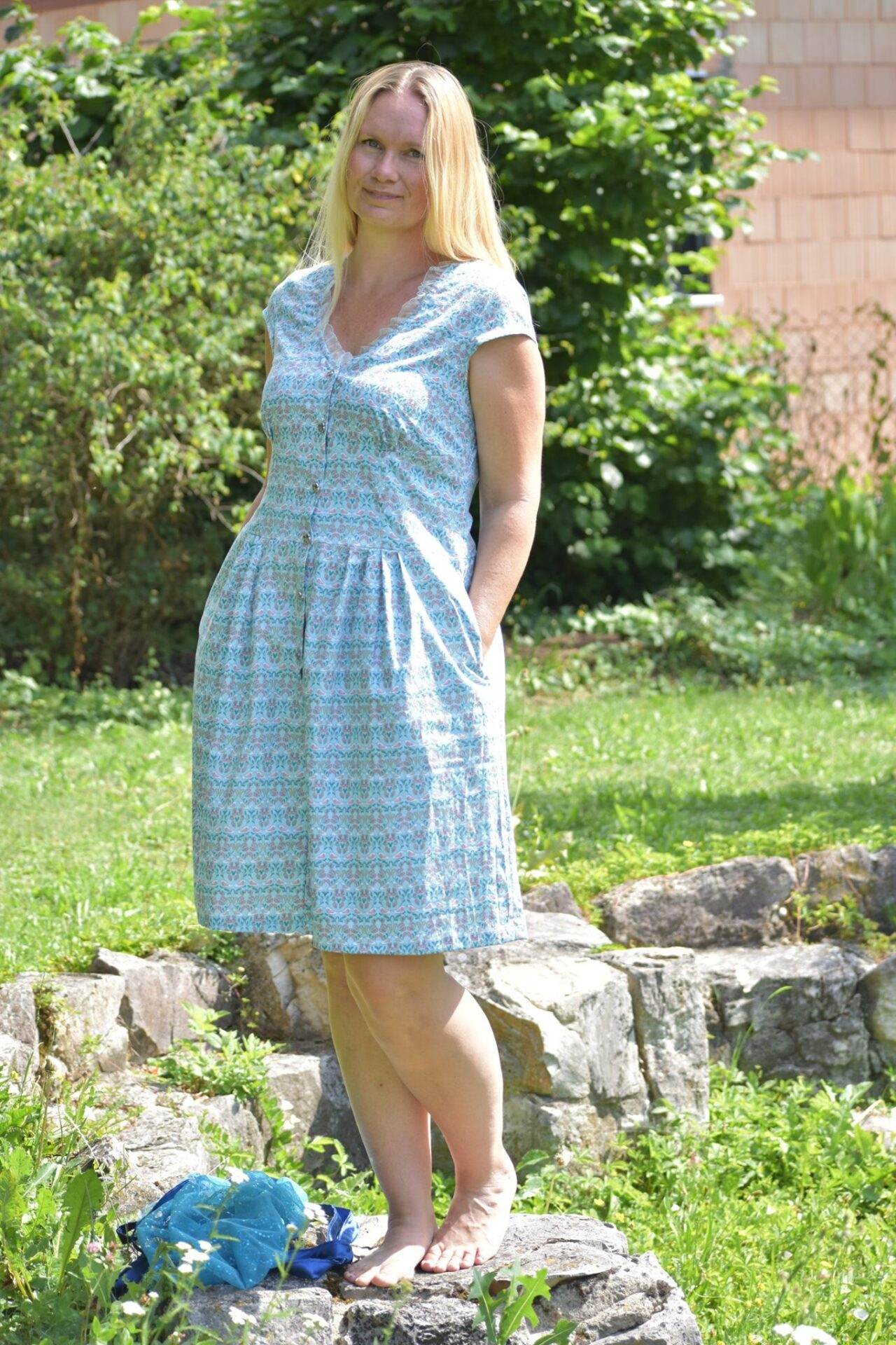 dirndlkleid sissi gr. 32 50 Frau im Sommerkleid steht im Garten auf Steinen.