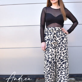 Frau in schwarzem Oberteil und Leopardenhose lächelt