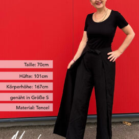 Person in schwarzer Kleidung vor rotem Hintergrund.