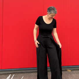 Person in schwarzer Kleidung vor roter Wand.