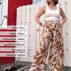 Frau in gemusterter Hose vor Holzzaun