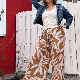 Frau in gemusterter Hose und Jeansjacke posiert im Garten.