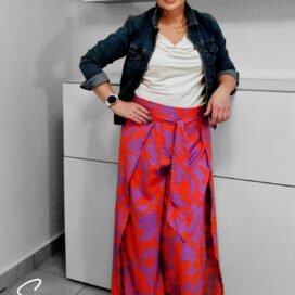 Frau trägt bunte Wickelhose mit floralem Muster nach Schnittmuster, kombiniert mit weißem Shirt, Jeansjacke und weißen Sneakern – modernes DIY-Outfit für Frühling oder Sommer."