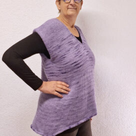 Frau in lila Strickoberteil vor Wand.