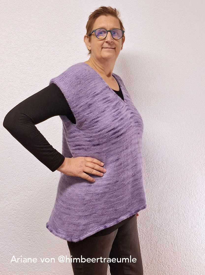 strickanleitung sweatervest lisbeth Frau in lila Strickoberteil vor Wand.