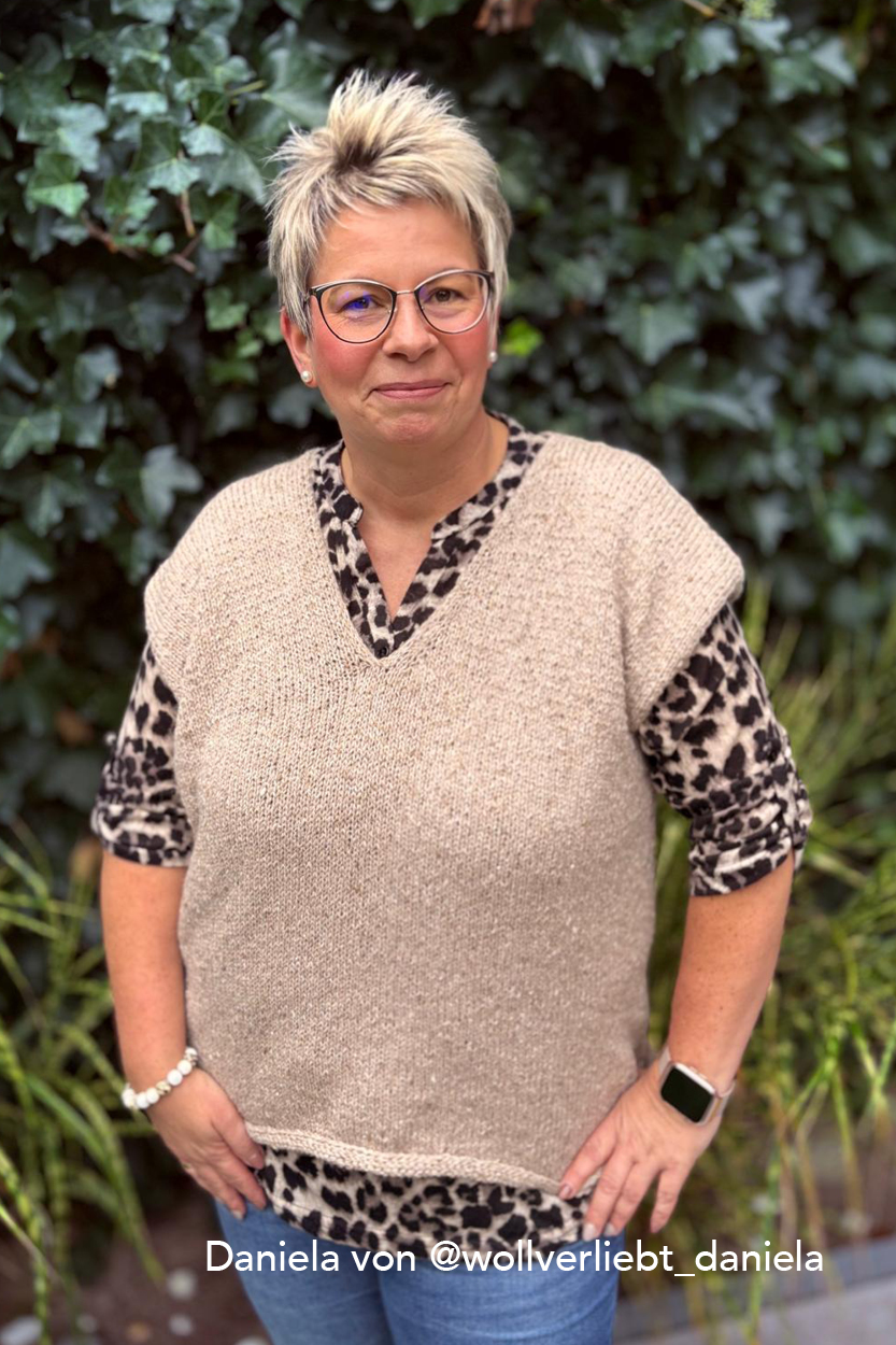 sweatervest lisbeth daniela2 Frau mit modischer Kleidung vor grüner Wand.