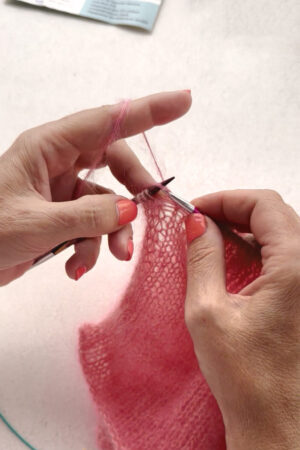 Hände stricken rosa Wolle mit Nadeln.